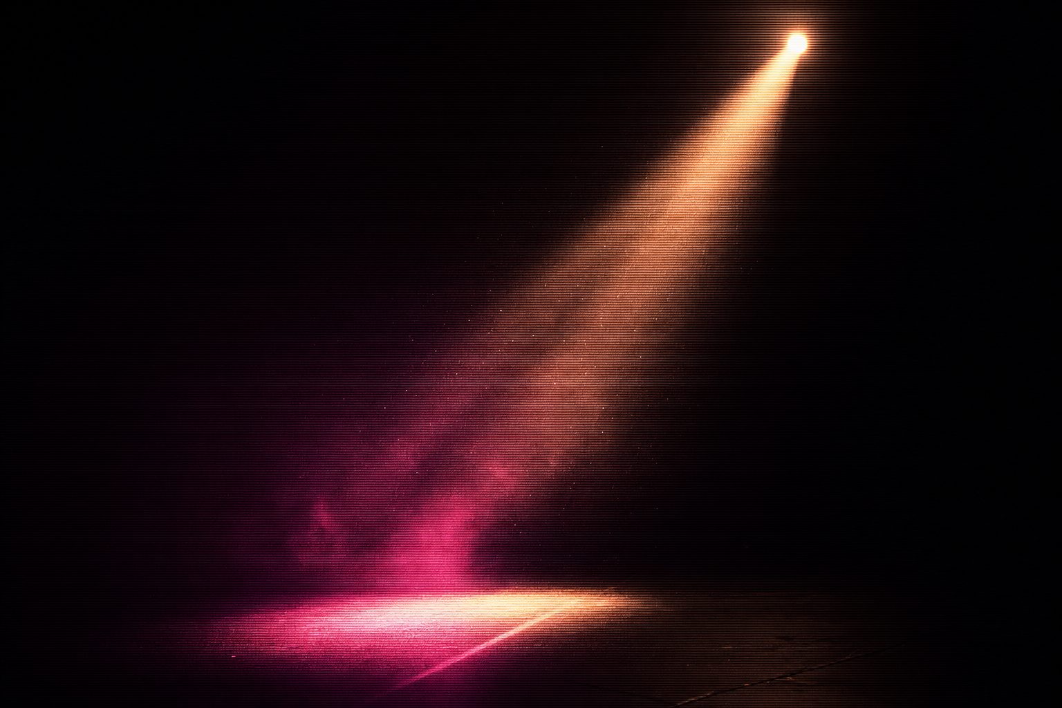 A single narrow beam of amber light sweeping slowly across an empty stage deck, dust visible in the throw.