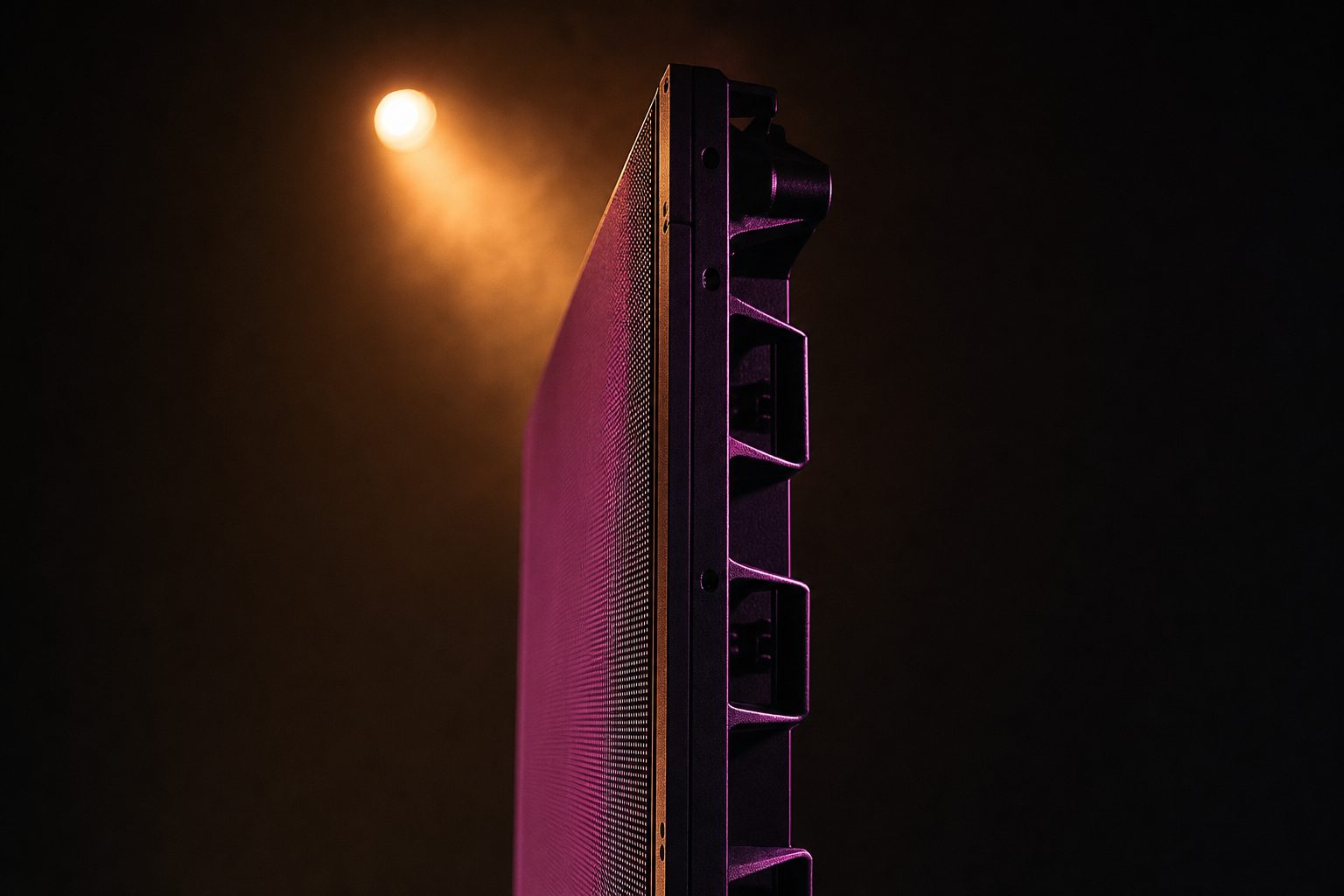 A single LED panel photographed edge-on so its physical thickness is visible, the diode face receding away from the lens into darkness, the frame and rear ribs catching a hard rim light.