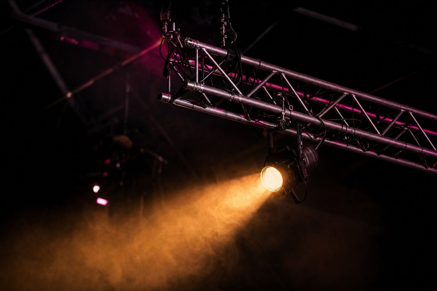 Bare truss geometry and rigging hardware against black, with one warm beam raking across the steel.