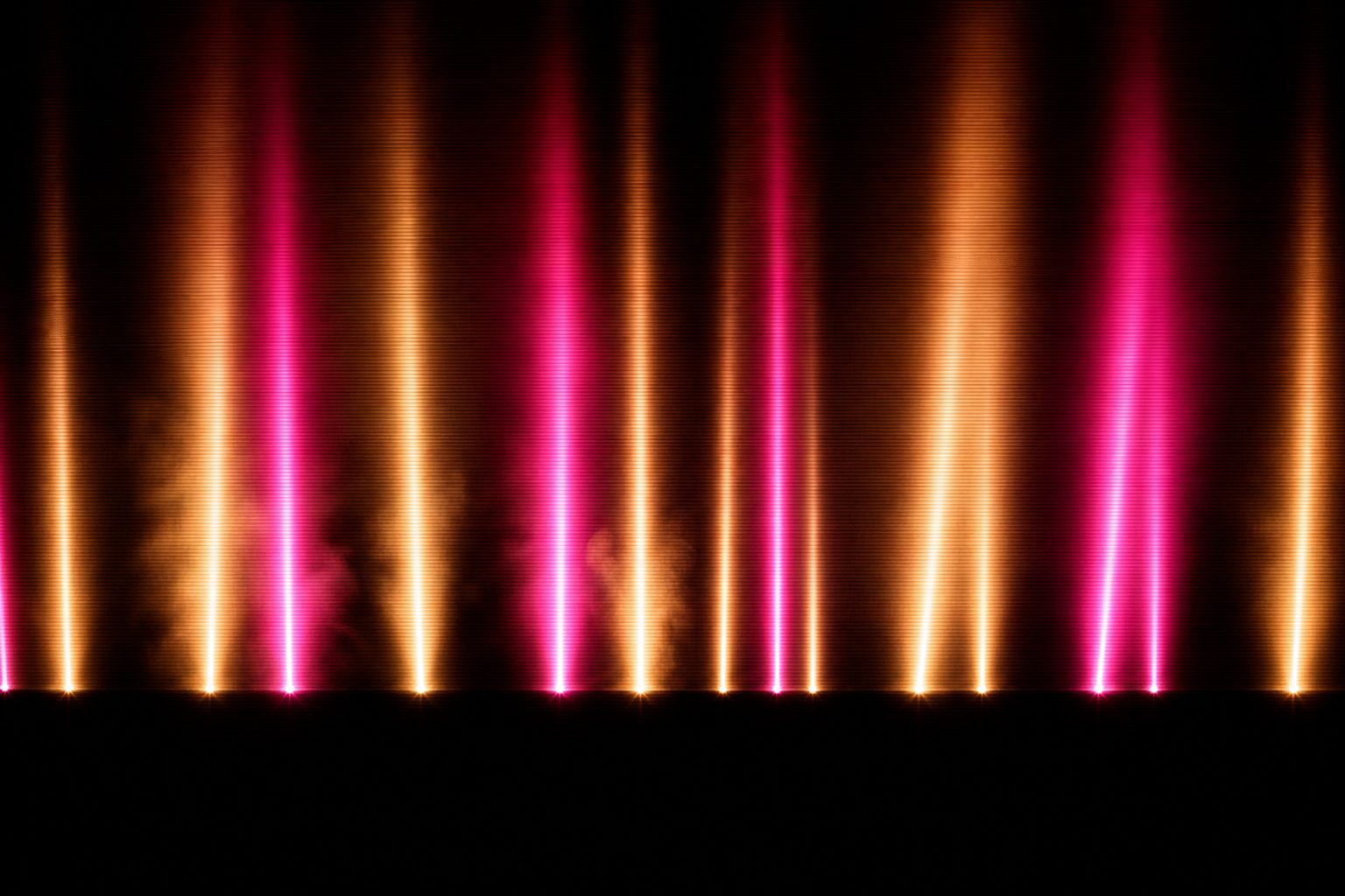 A low horizon with vertical columns of magenta and amber light standing against a black night sky.
