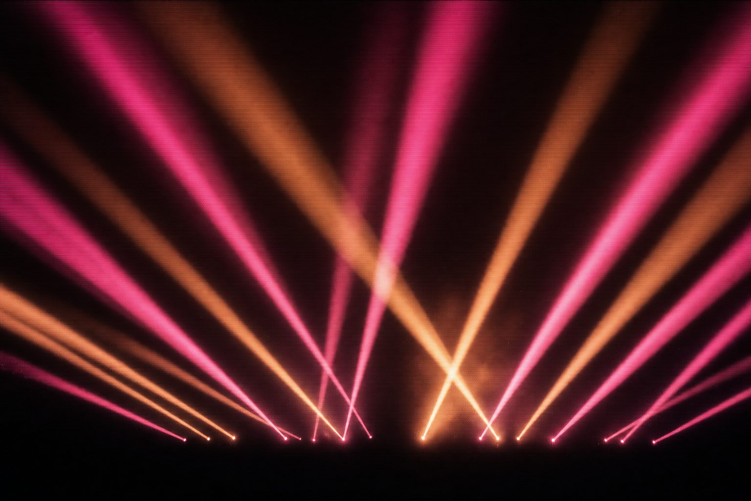 A wide field of magenta and amber beams fanning out over an open night sky, dust visible in the air.
