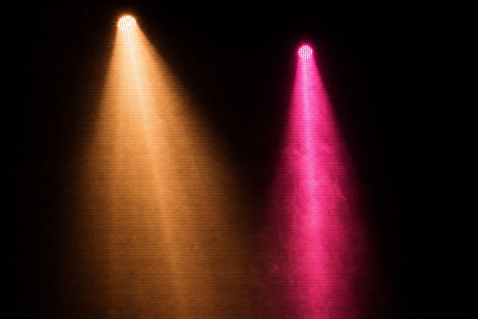 Two columns of light at different depths, one warm amber and one magenta, standing in dark space.