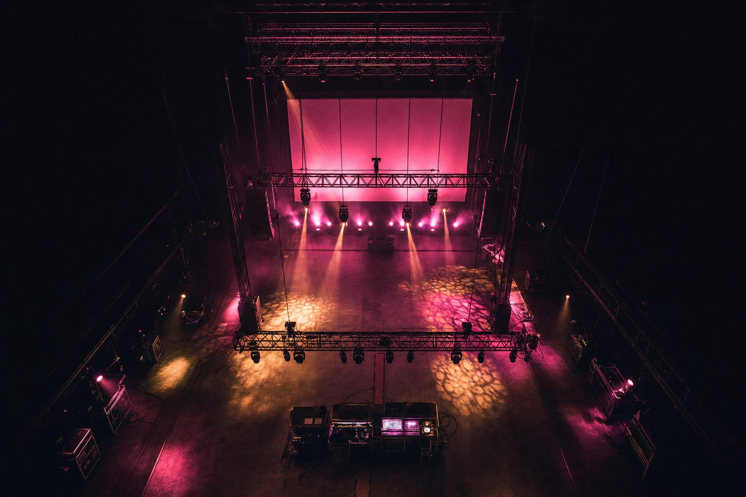An empty dark venue seen from high at the back, the whole rig laid out below in one view: truss lines, a screen plane, lighting positions and cable runs all legible at once.